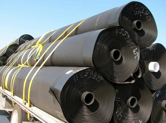 Large rolls of black industrial HDPE Pond Liners material are stacked and secured with yellow straps on a flatbed trailer.